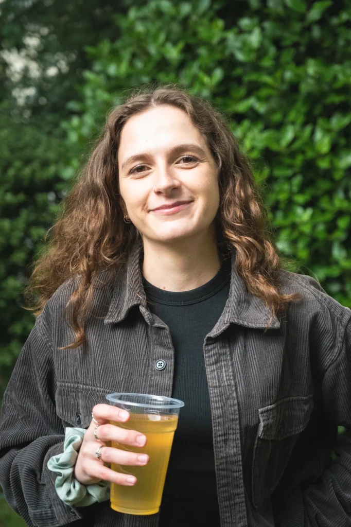 Woman with wavy brown hair holding a drink and smiling